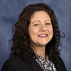 headshot of a smiling woman with curly dark hair dressed in business professional attire